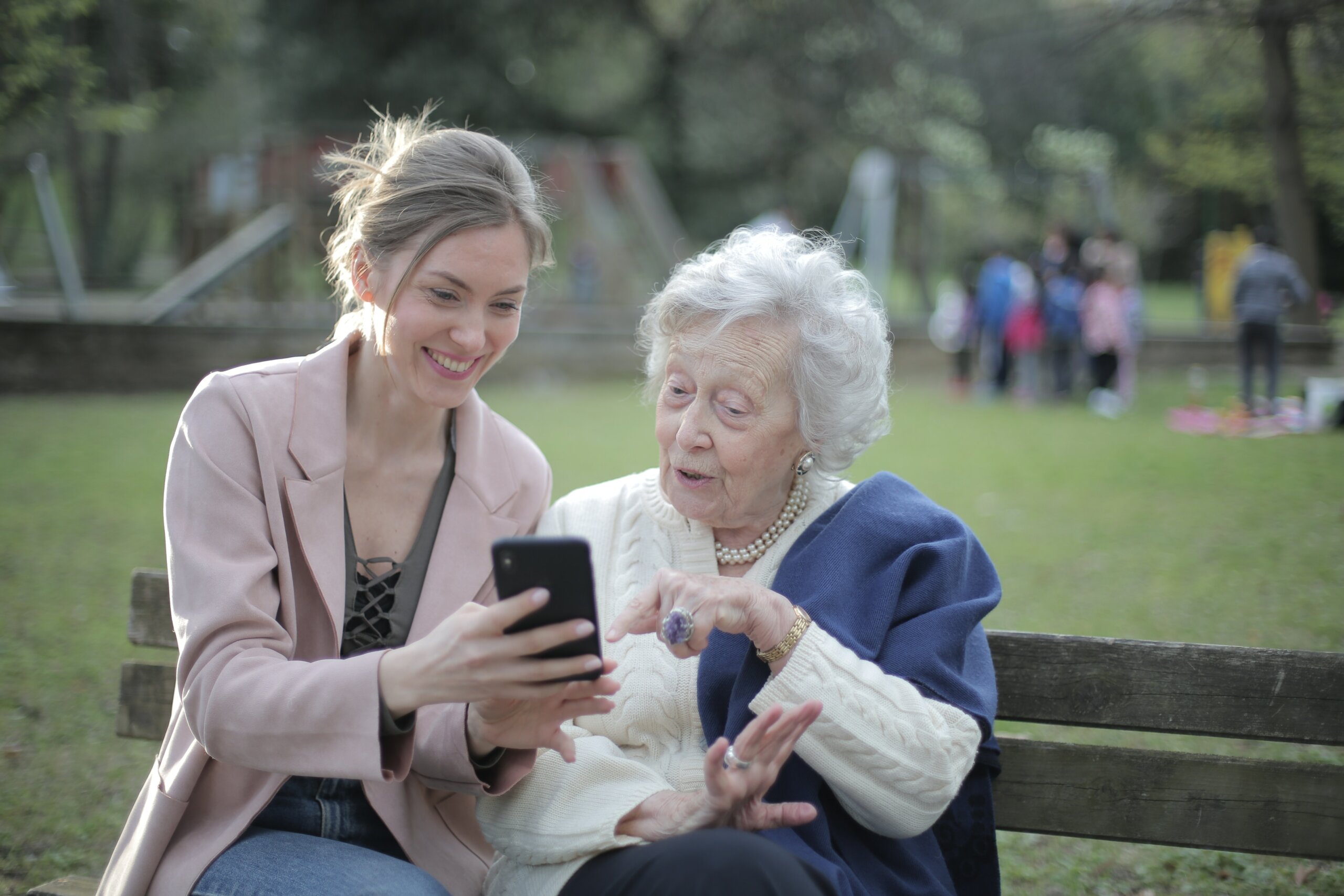 Daughter showing her grandmother Trayt.Health platform on her mobile device sitting on a park bench